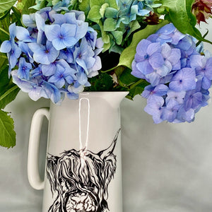 White bone china jug with stylised highland cow design, filled with blue hydrangeas