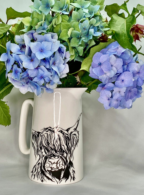 White bone china jug with stylised highland cow design, filled with blue hydrangeas